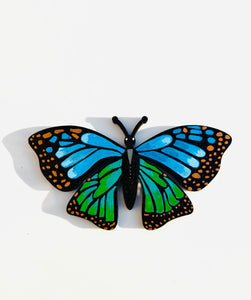 Butterfly-shaped magnet with blue and green wings on a white background