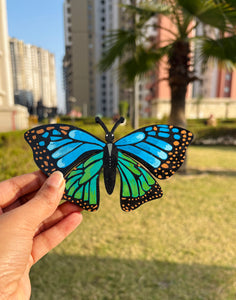 Hand holding a colorful butterfly-shaped magnet with a cityscape in the background