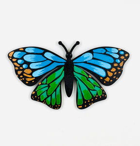 Butterfly-shaped magnet with blue and green wings on a white background
